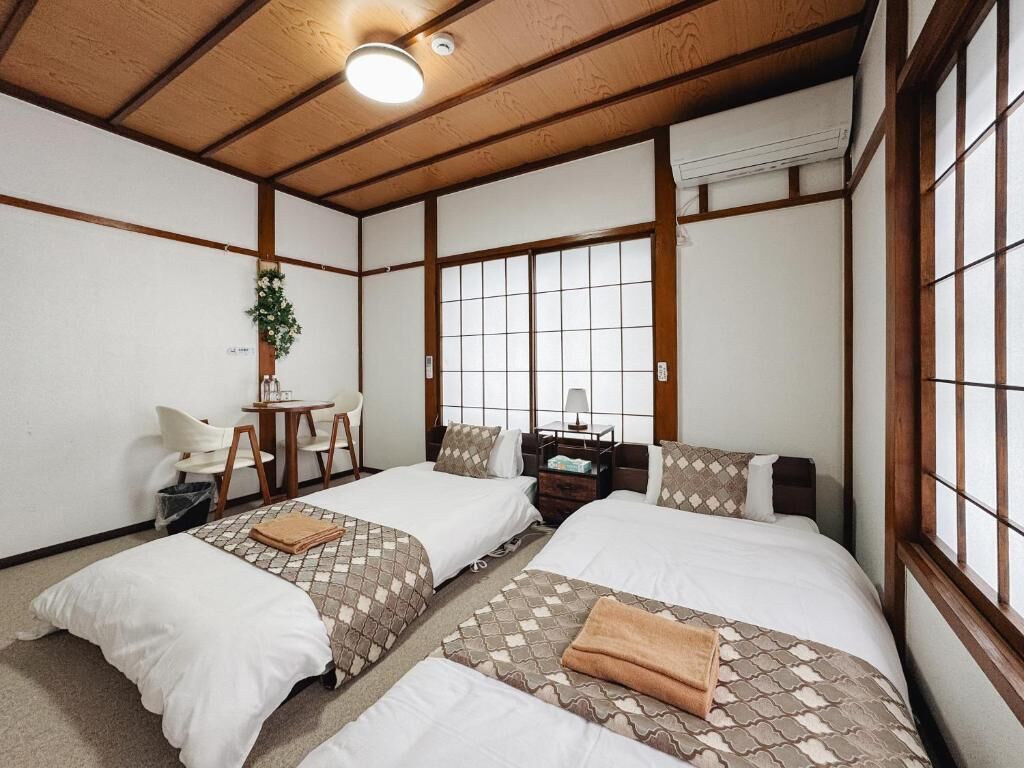 A traditional Japanese-style room with two beds, a small desk, and a window with a grid pattern.