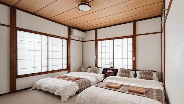 Een traditionele Japanse kamer met twee bedden, houten balken, tatami vloerbedekking en grote ramen.