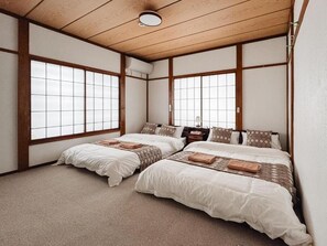 Et traditionelt japansk værelse med to senge, træbjælker, tatamimåtter og store vinduer.