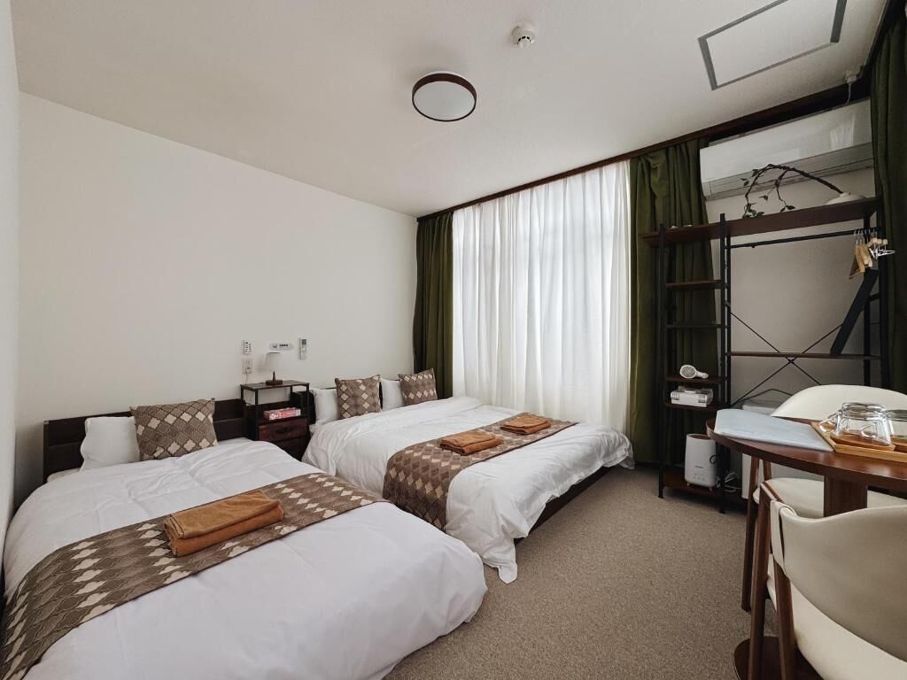 A hotel room with two beds, a desk, a chair, a wardrobe, and a window with curtains.