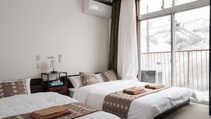 Een hotelkamer met twee bedden, een nachtkastje, een airconditioning en een raam met uitzicht op een besneeuwd landschap.