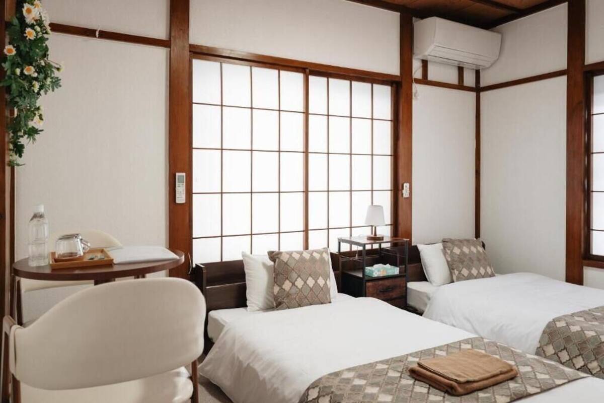Une chambre d’hôtel avec deux lits, une petite table avec une lampe, une chaise et une fenêtre donnant sur un beau paysage.