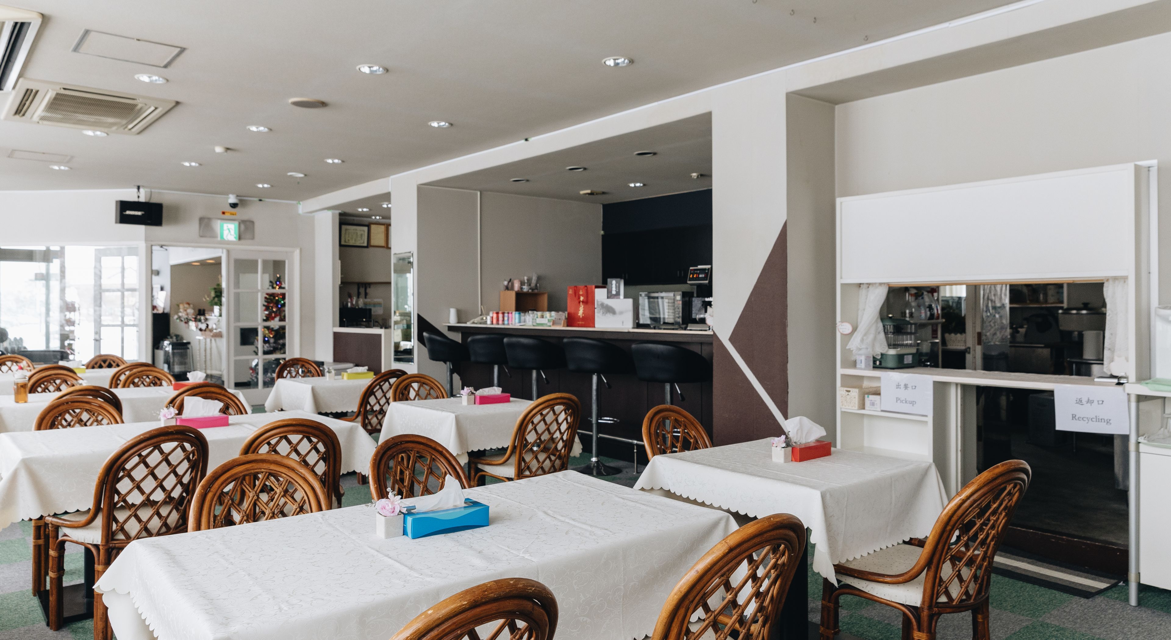 A dining area with tables and chairs, a kitchen area, and a sign indicating a recycling bin.