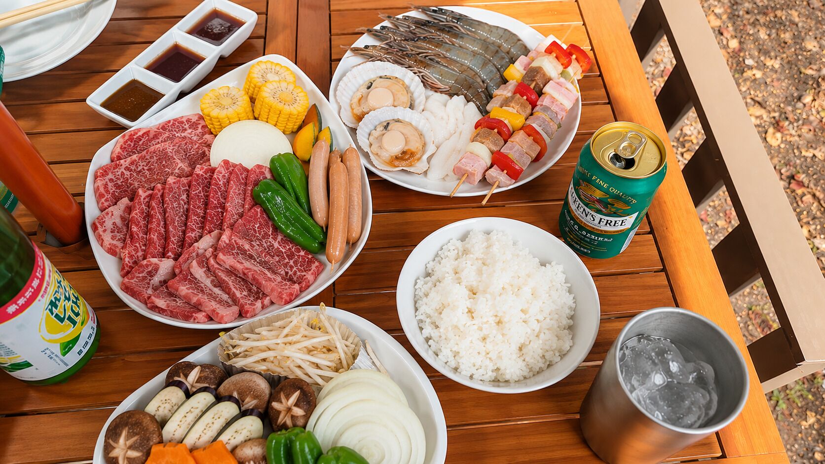 A wooden table with various food items including meat, vegetables, rice, and a can of beer.