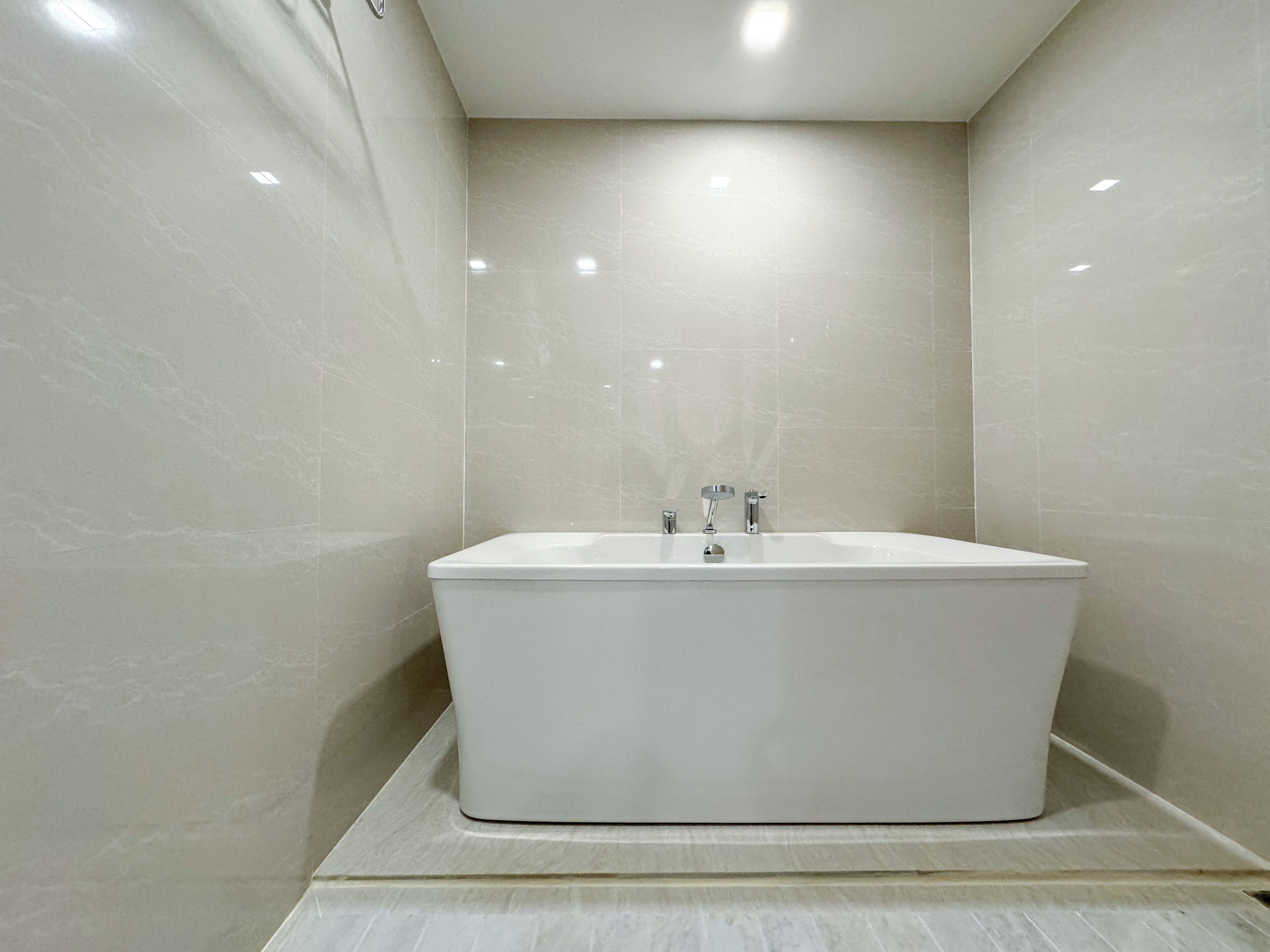 A modern bathroom with a freestanding bathtub, tiled walls, and recessed ceiling lighting.