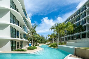 A modern hotel with a swimming pool, palm trees, and a clear blue sky. - SeaView Stay Walk to Waterpark Town C137 (Rawai)