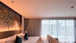 Ein Hotelzimmer mit einem großen Bett, einer Couch, einem Schreibtisch und Blick ins Freie durch transparente Vorhänge.