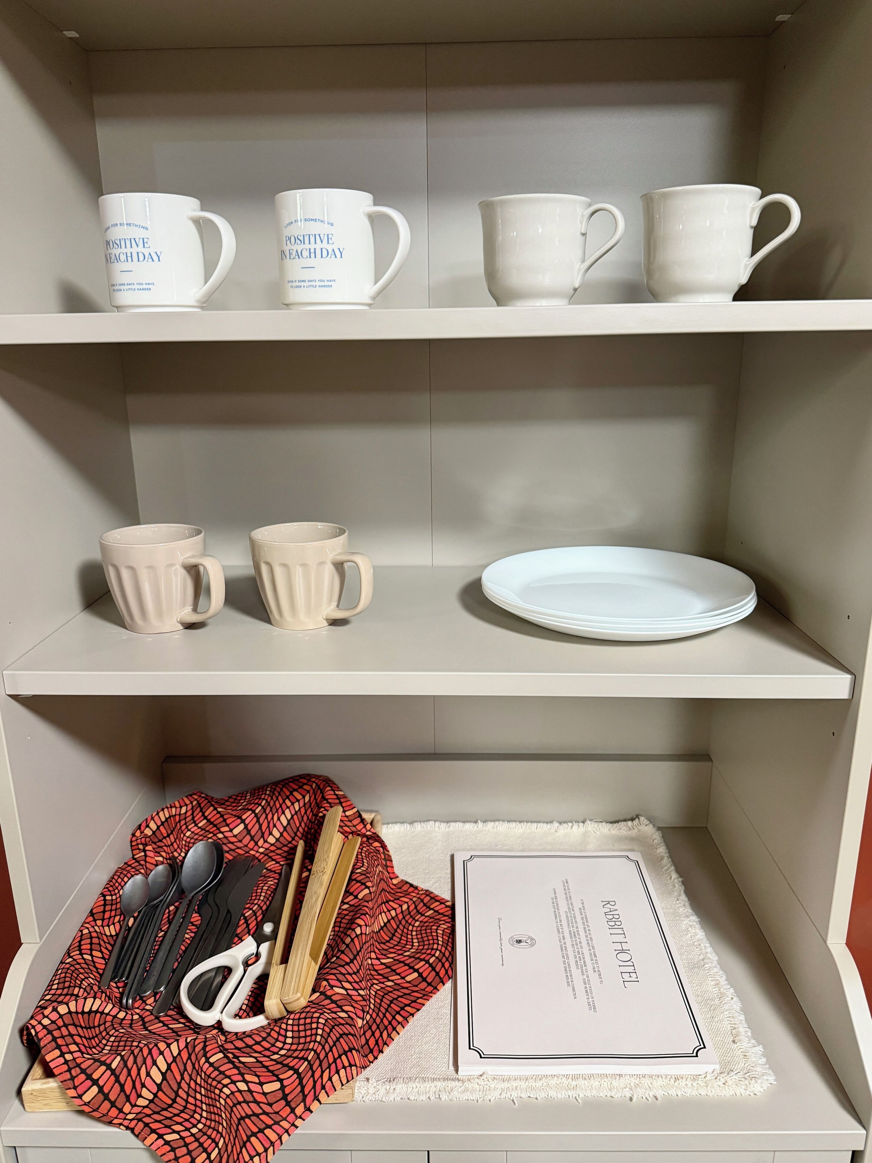 Een plank met witte mokken en een bord, een rood geruit kleedje met bestek, en een certificaat op een witte onderzetter.