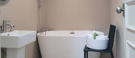 Un baño moderno con una bañera independiente, un lavabo y una silla con artículos de aseo.