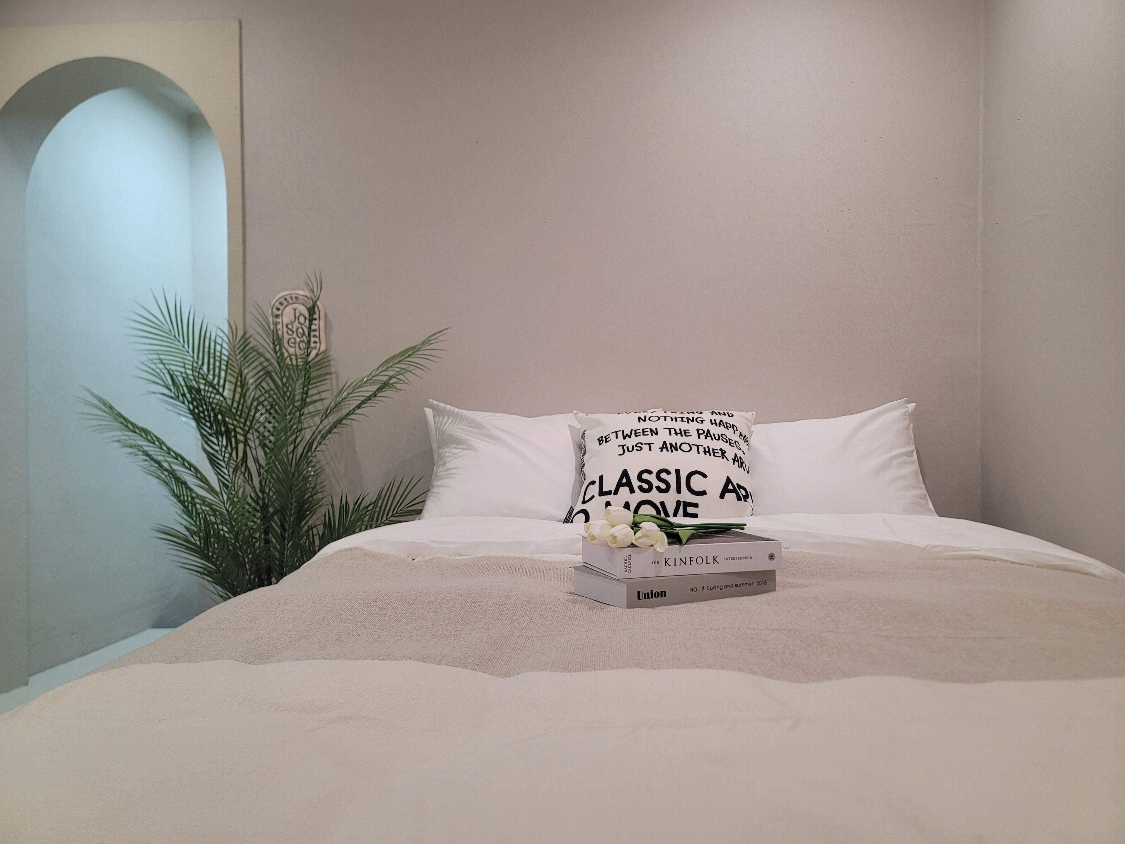 Een bed met een wit kussen, een boek en een boeket witte bloemen.