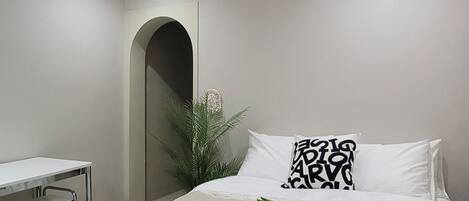 A modern bedroom with a bed, a desk, and a plant.