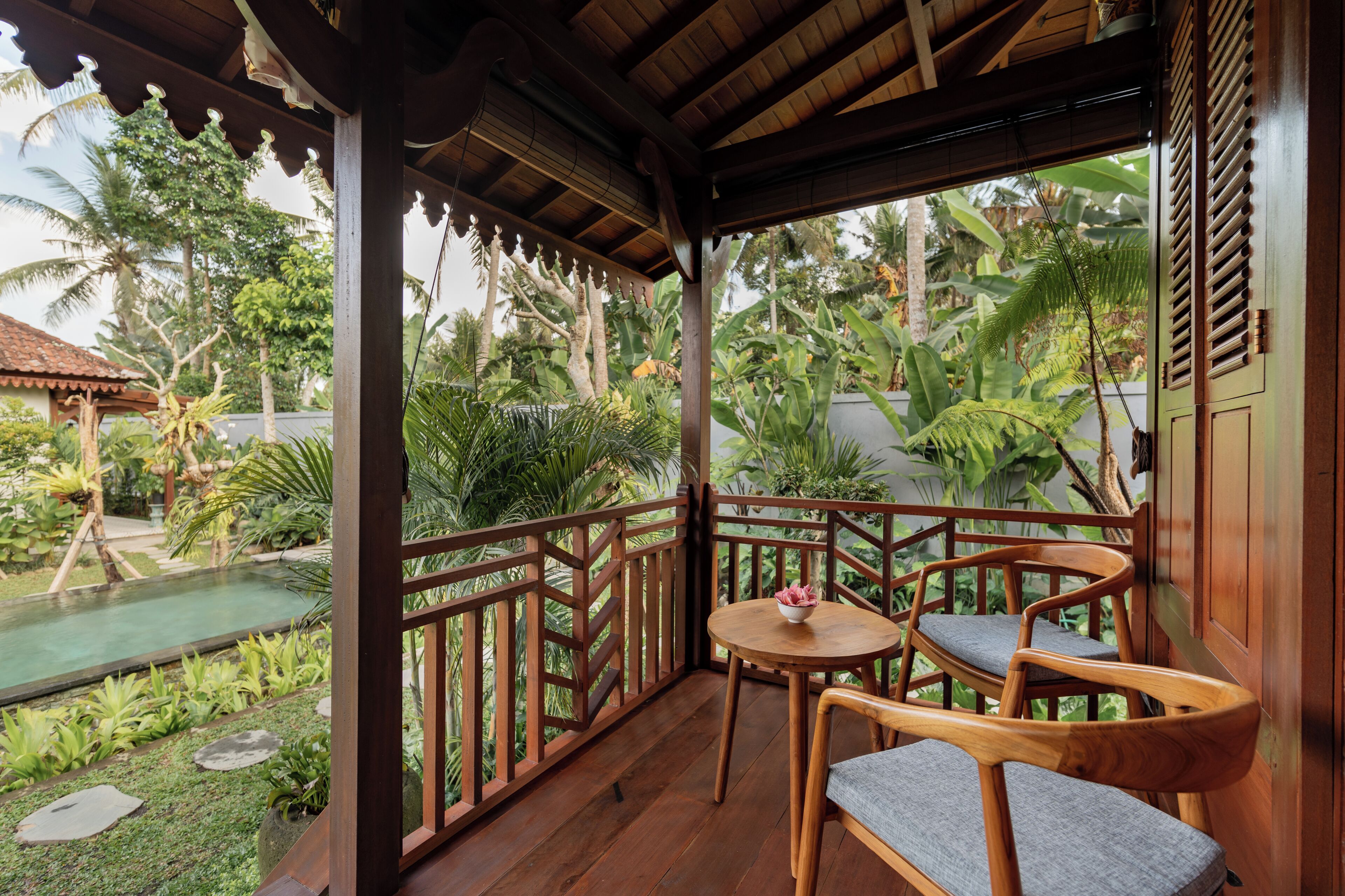 A wooden balcony with a view of a garden and a pool.
