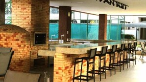 Un espace bar doté d’une cheminée en briques, de tabourets de bar et d’une grande fenêtre donnant sur une piscine.