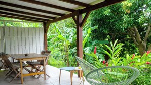 Une terrasse extérieure avec une table et des chaises en bois, entourée d’une végétation luxuriante et agrémentée d’une pergola en bois.