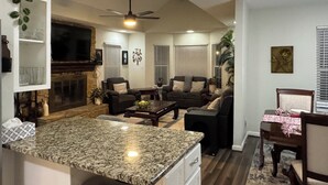 A modern living room with a fireplace, a ceiling fan, and a dining area with a granite countertop. - Convenient, cozy home surrounded by trees, 6 miles to BNA, 13 miles to downtown. (Hermitage)