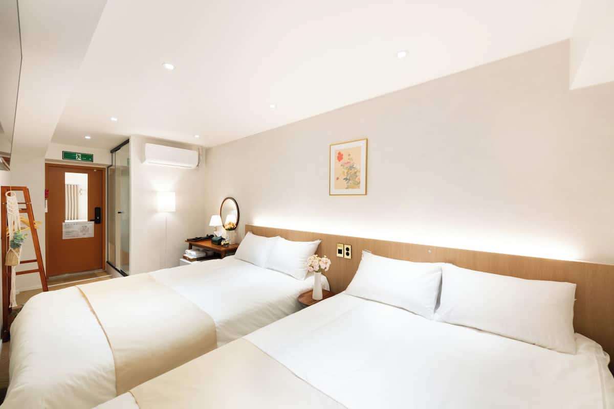 A hotel room with two beds, a wooden headboard, a bedside table with a lamp, a mirror, and a framed picture on the wall.