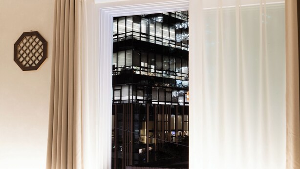 Habitación de hotel con un ventanal grande, vista a un edificio con balcones y un elemento decorativo octogonal en la pared.