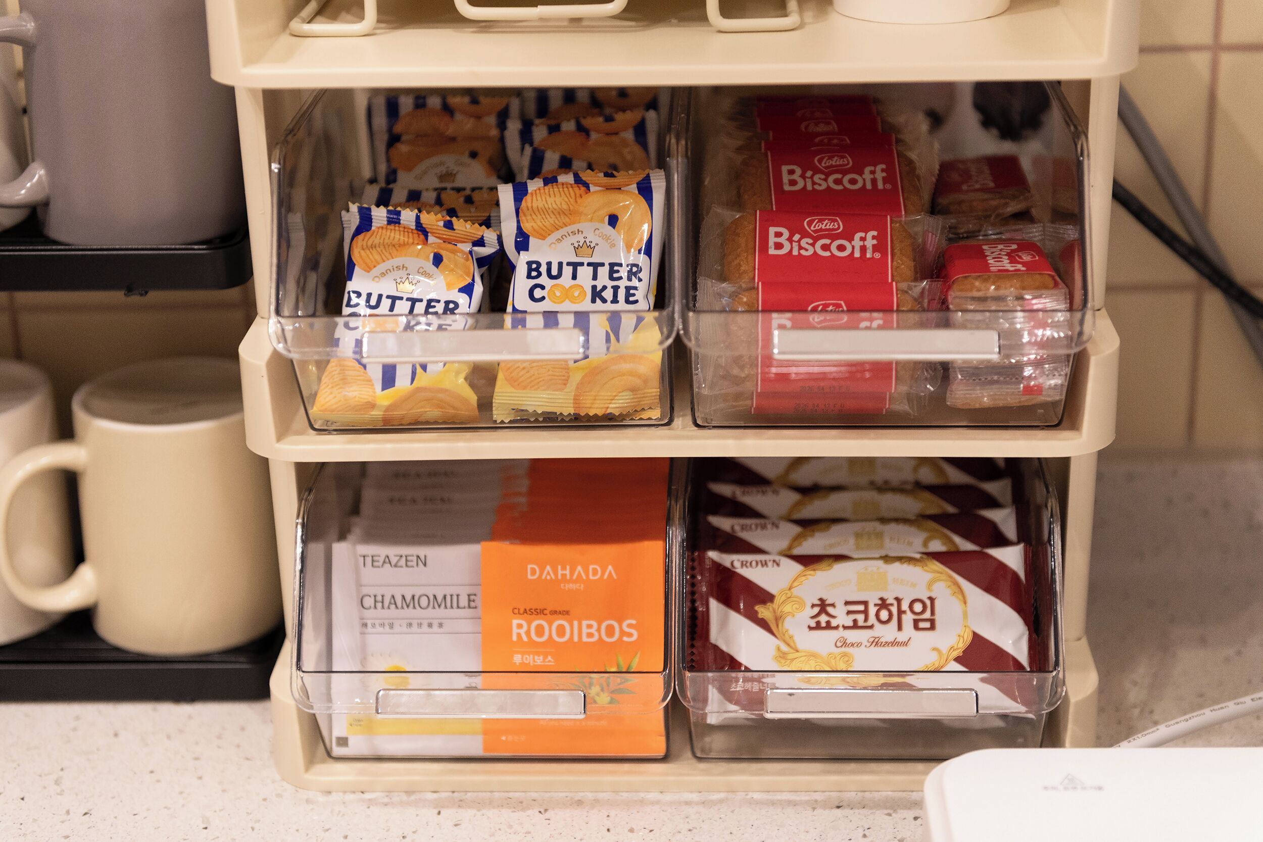A shelf with various packaged snacks and beverages, including butter cookies, biscuits, rooibos tea, and chocolate.