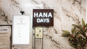 Un área de recepción con pared de mármol, un letrero 'HANA DAYS', un KIOSK para el registro y un código QR para acceso a Wi-Fi.