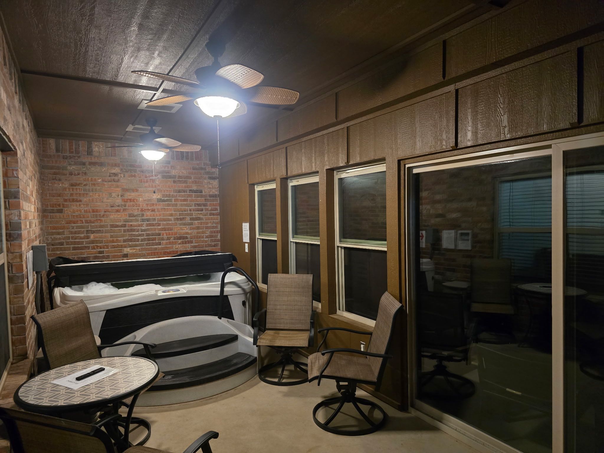 A cozy indoor space with a brick wall, a ceiling fan, and a large window.