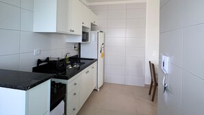 A narrow kitchen with white cabinets, a black countertop, and a microwave.