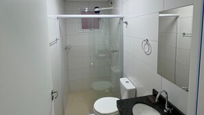 A modern bathroom with a glass-enclosed shower, a white toilet, a black sink, and a mirror above the sink.