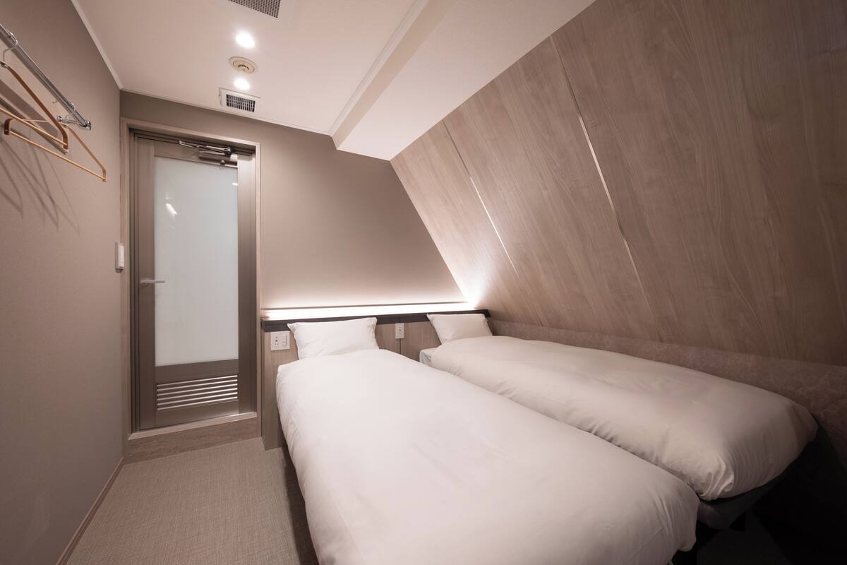 A small, modern hotel room with two single beds, a wooden accent wall, and a door leading to a bathroom.