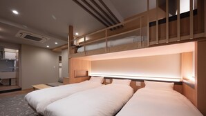 Habitación de hotel moderna con dos camas individuales, una litera de madera encima, un escritorio y un baño con ducha.