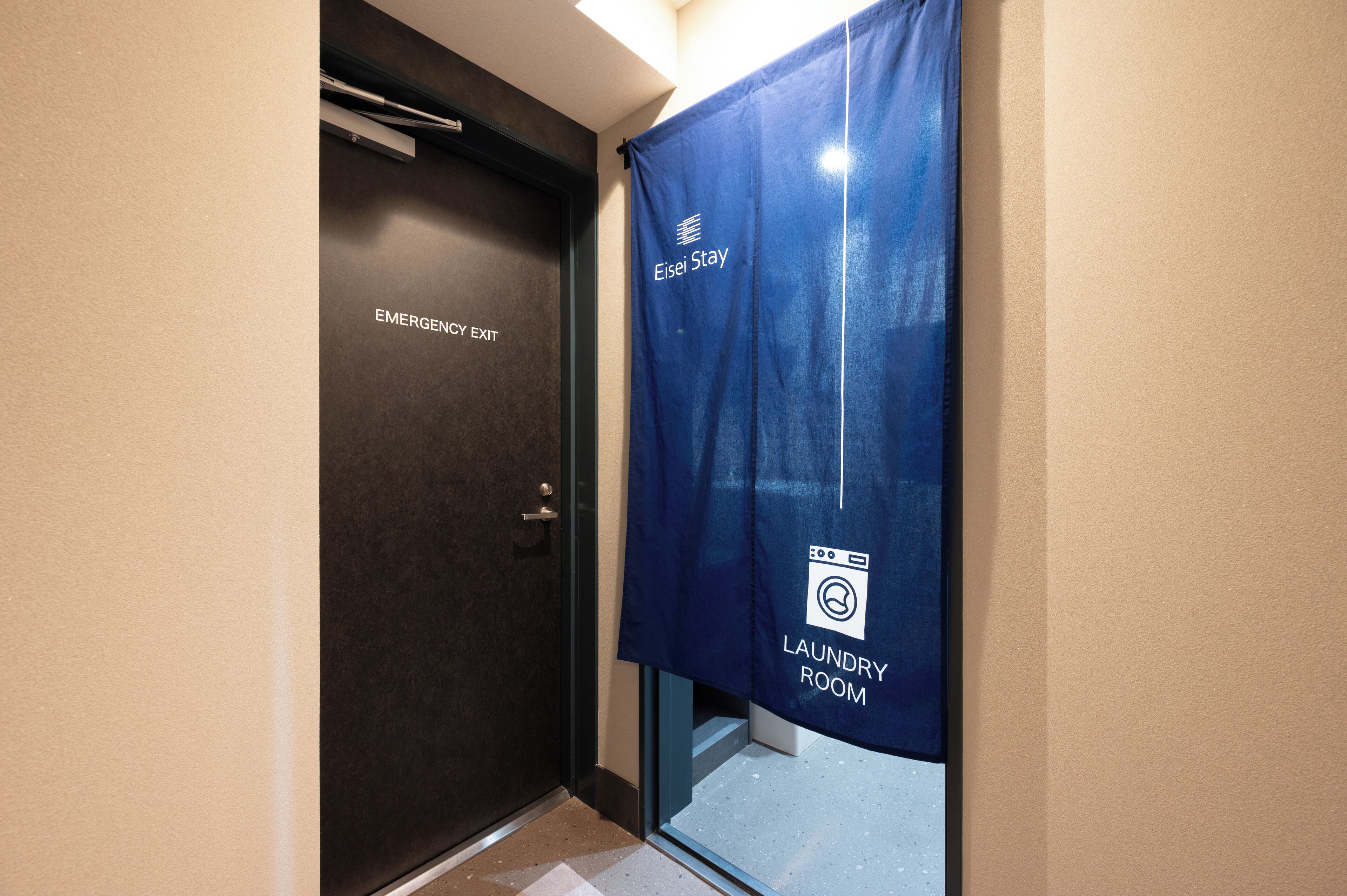 A hotel room with an emergency exit door and a blue curtain indicating a laundry room.
