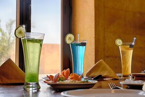 Ett bord med tre färgglada drinkar, en tallrik med mat och en pyramidformad dekoration i trä.