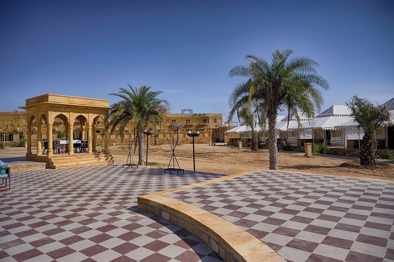 A courtyard with a checkered floor, a pavilion, palm trees, and traditional buildings.