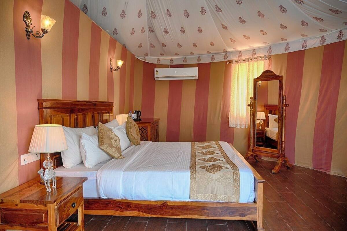 Una camera d'albergo con un letto grande, una testiera in legno, un comodino con una lampada, uno specchio e carta da parati a righe.