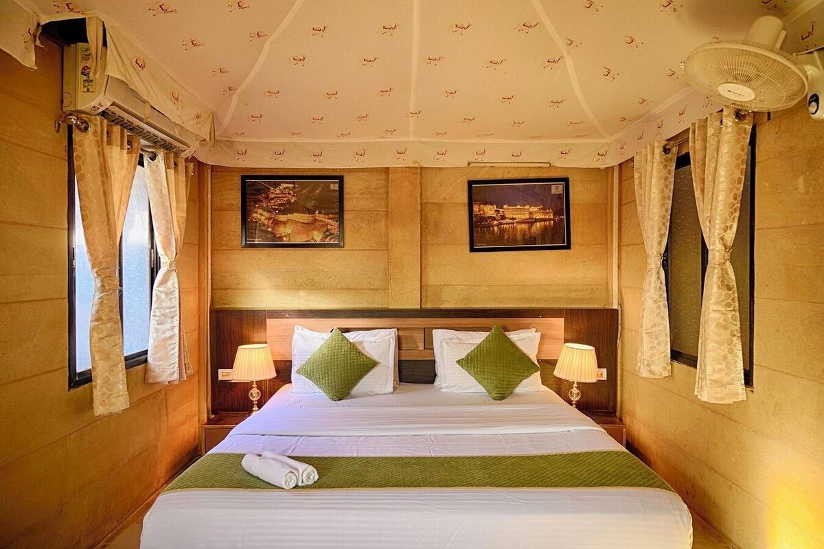 Camera d'albergo con un letto grande, due climatizzatori a parete, due quadri appesi e una ventola a soffitto.