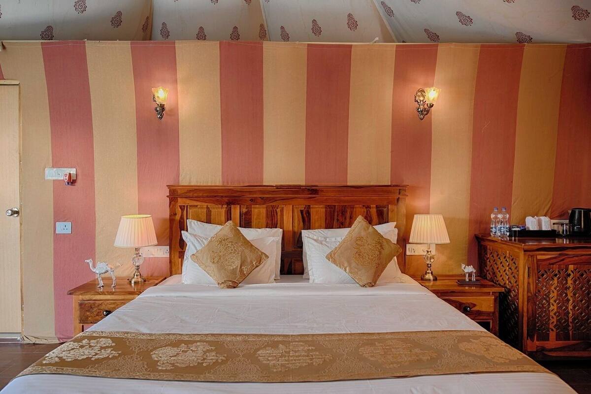 Una camera d'albergo con un letto grande, due lampade ai lati del letto, un poggiatesta in legno e carta da parati a righe.