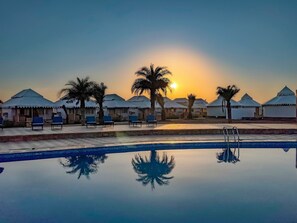 A poolside view with a clear sky, palm trees, and white-roofed structures. - Desert Valley Resort (Jaisalmer)