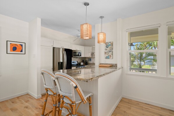 A kitchen with a central island, white cabinetry, a stainless steel refrigerator, and a window with a view of palm trees.