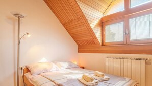 A bedroom with a sloped ceiling, a bed with a striped bedspread, two towels on the bed, a floor lamp, and a window with blinds. - Farm Stay Oblak Studio Ina + Shared Sauna, Ortnek, Slovenia (Ortnek)