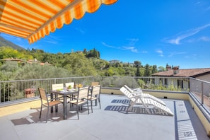 A terrace with a table set for dining, chairs, and a sunshade.