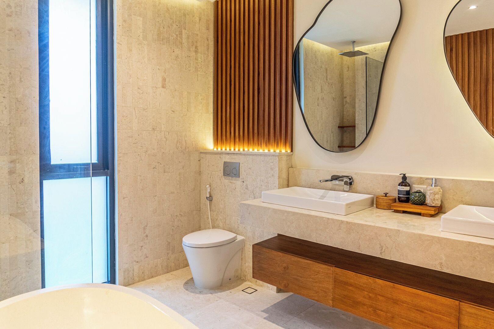 A modern bathroom with a large bathtub, two sinks, a toilet, and a vanity with a mirror.