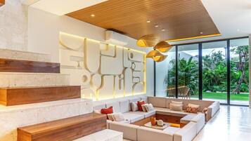 A modern living room with a wooden staircase, a sectional sofa, and a wall with abstract light fixtures.