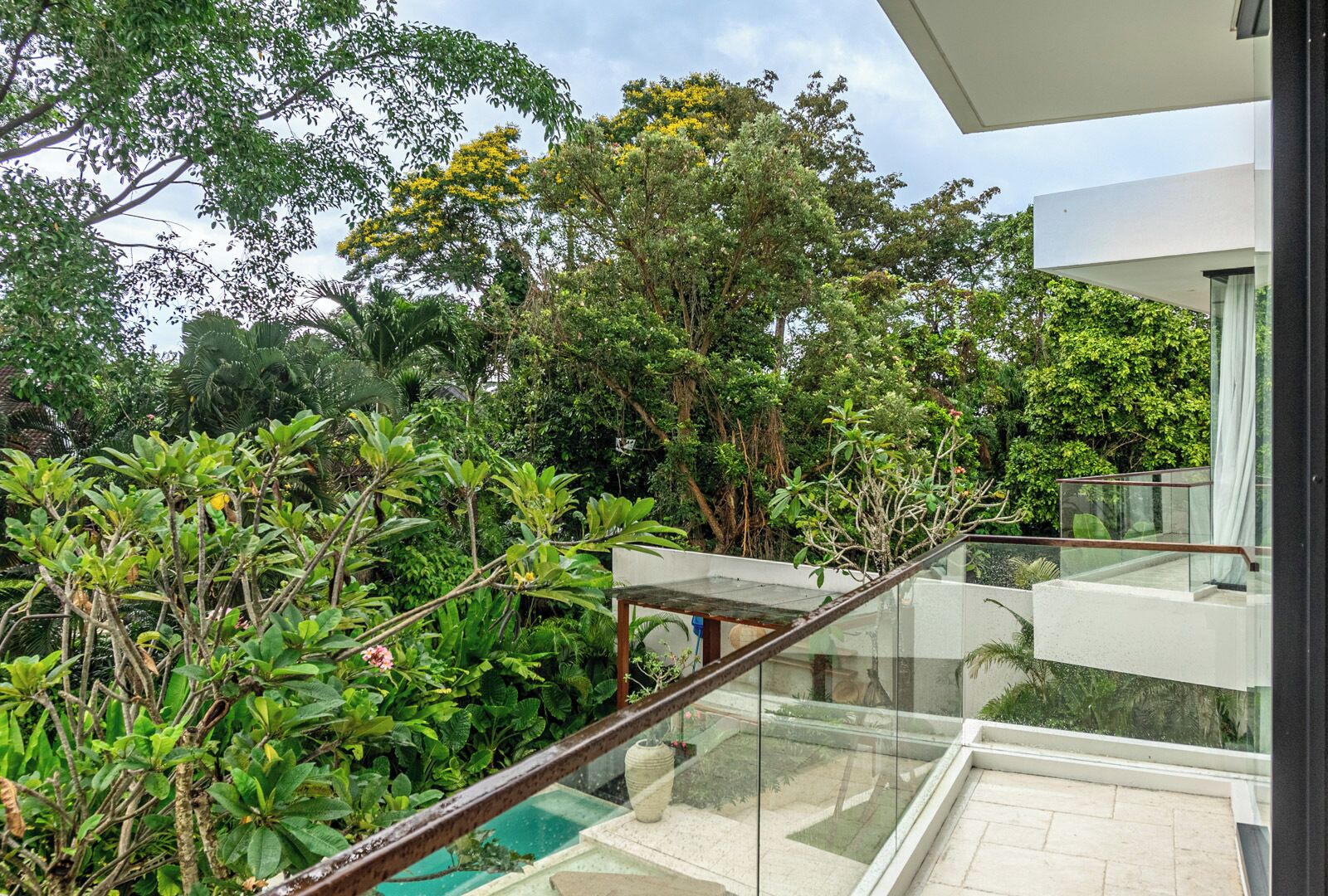 A modern balcony with glass railings overlooking a lush garden and a clear sky.