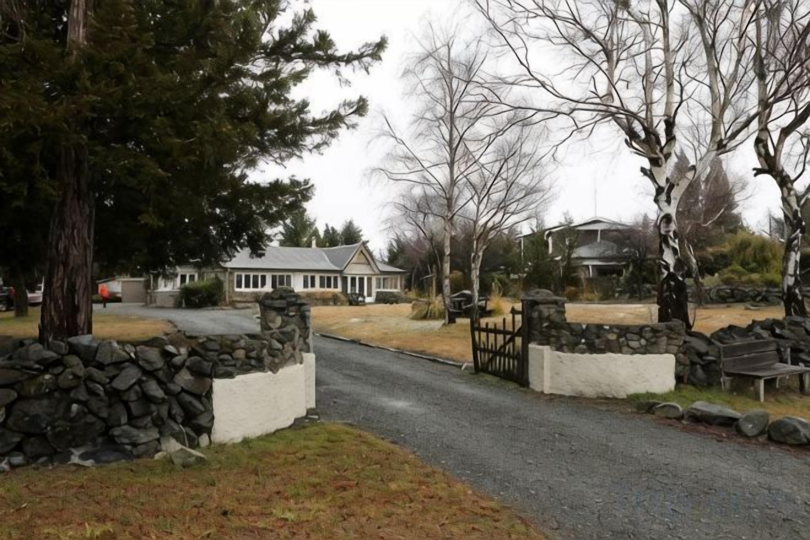 A residential driveway with a stone wall, a wooden gate, and a house in the background.