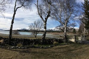 A landscape with trees, a stone wall, and a view of a lake and mountains. - Tekapo1929 Lakefront Villa (Lake Tekapo)
