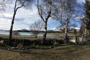 Un paisaje con árboles, un muro de piedra y vistas a un lago y montañas.