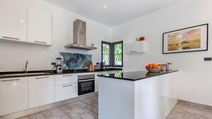 Une cuisine moderne avec des meubles blancs, un îlot central et une grande fenêtre.
