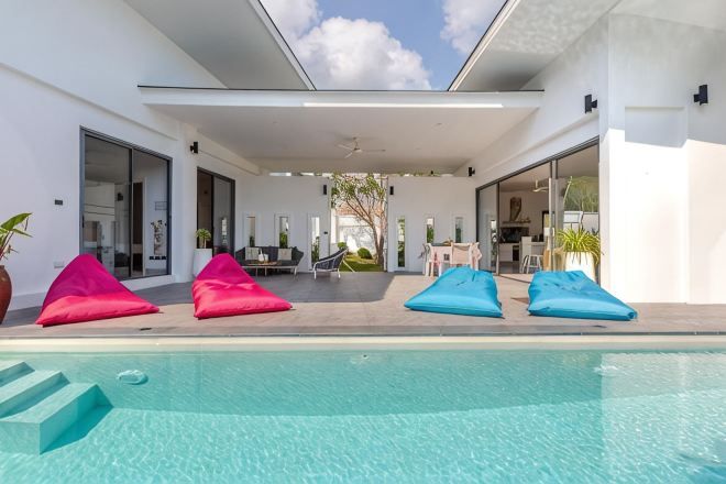 An outdoor swimming pool area with lounge chairs, a covered patio, and a view of the interior.
