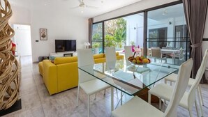 Un salon moderne avec une table à manger en verre, un canapé jaune et un téléviseur.