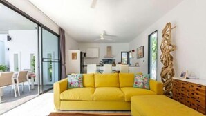 Un canapé jaune vif agrémenté de coussins à motifs floraux, dans un salon moderne avec une table basse en bois et un ordinateur portable posé dessus.