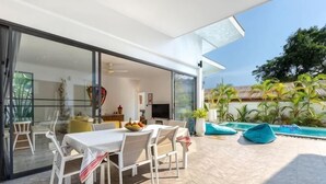 Un espace extérieur aménagé pour les repas, avec une table et des chaises, une piscine et une porte vitrée donnant sur un espace de vie.