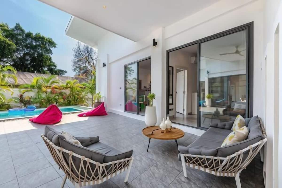 A modern outdoor patio with wicker furniture, a round table, and a glass door leading to an indoor area.